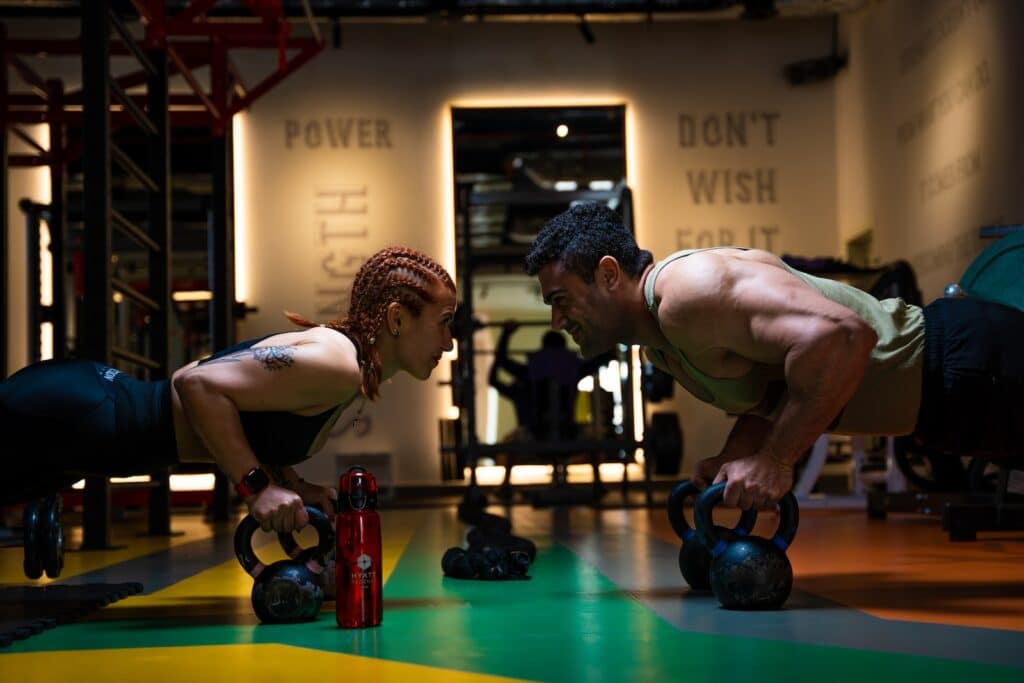 a man and a woman doing push ups with kettles HIIT