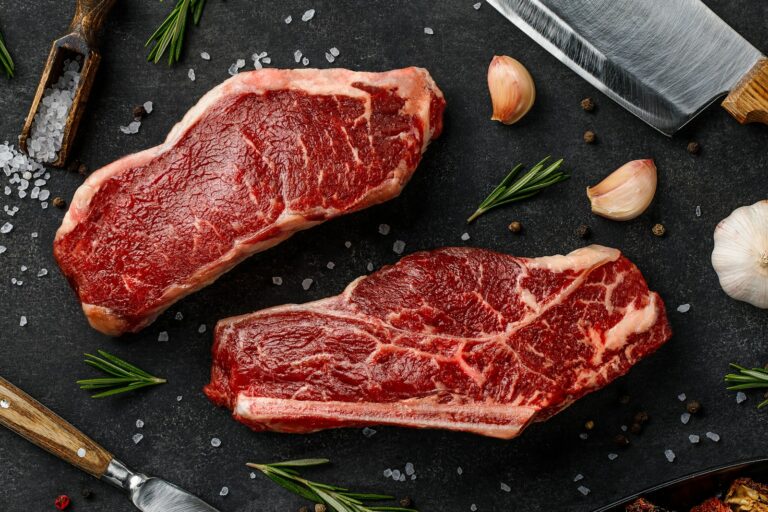 two steaks on a cutting board next to garlic, garlic, and a knife