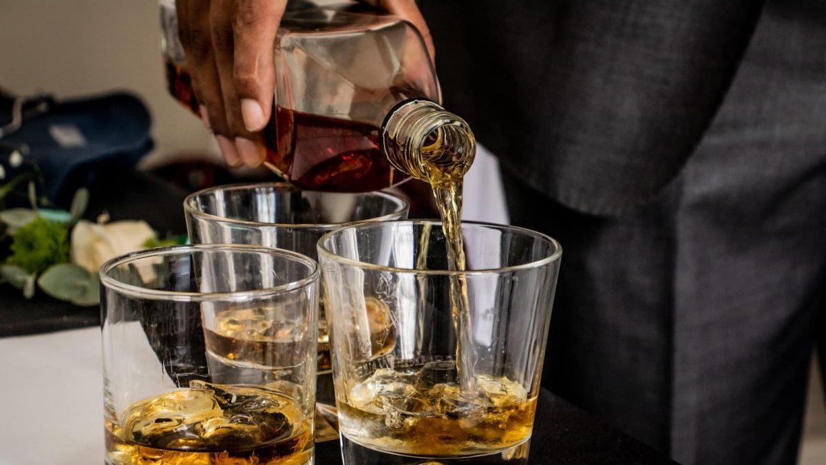 person pouring brown liquid on clear drinking glass